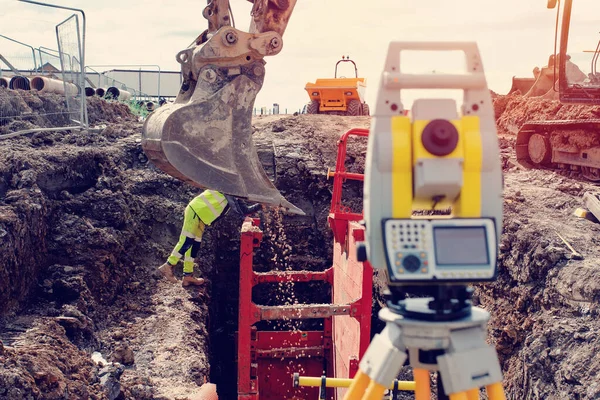 stock image Deep drainage excavation works, with red trench support box installed into the trench and yellow total station next to it