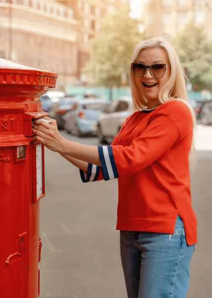 woman in red short posting letters in red post box in England