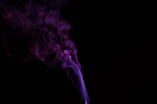 Incense stick with smoke against black background