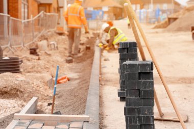 İnşaatçılar yol ve patika inşaatı sırasında yarı beton karışımına kaldırım blokları kuruyorlar. Kaldırımları engelleme işlemi devam ediyor
