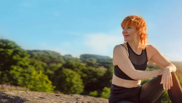 happy red woman in sports suit sitting on a cliff after exercises