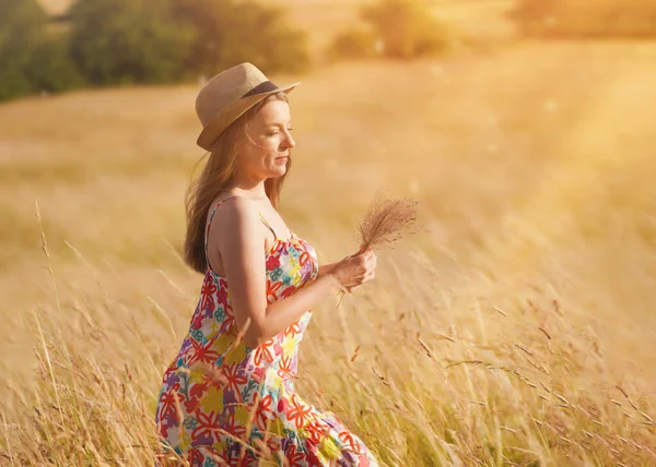woman in dress and hat walking in a wheat field in summer