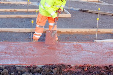 İnşaatçı bir kürekle beton döktü. Bir inşaat işçisi resmi işlere renkli beton koyuyor.