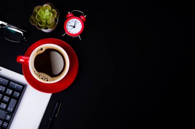 red cup of coffee, pen, glasses, alarm,  plant, phone, and paper on a black background  as workplace top view space for text