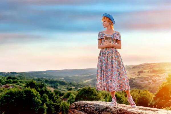 woman in a dress and a hat with a lavender bouquet in her hands on a hill in summer sunset