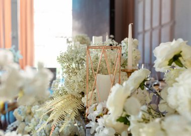 Modern düğünde cam cam lüks bir masada yakın plan altın mum tutacağı. Şenlikli masa dekoru. Çiçekler, şeffaf cam ve altın dekor, mumlar. Yan görünüm bokeh arkaplanı