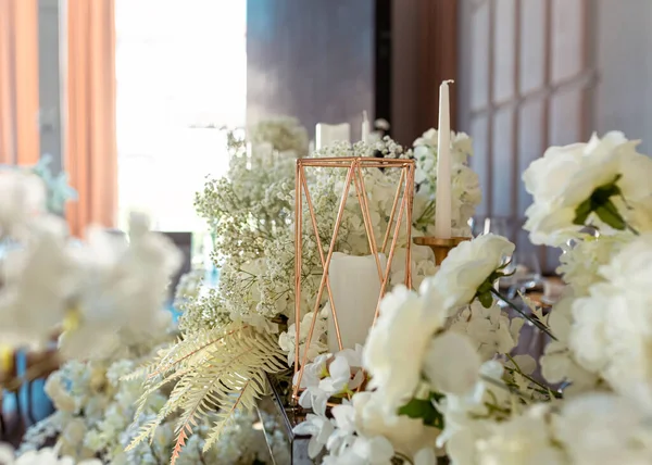 Modern düğünde cam cam lüks bir masada yakın plan altın mum tutacağı. Şenlikli masa dekoru. Çiçekler, şeffaf cam ve altın dekor, mumlar. Yan görünüm bokeh arkaplanı