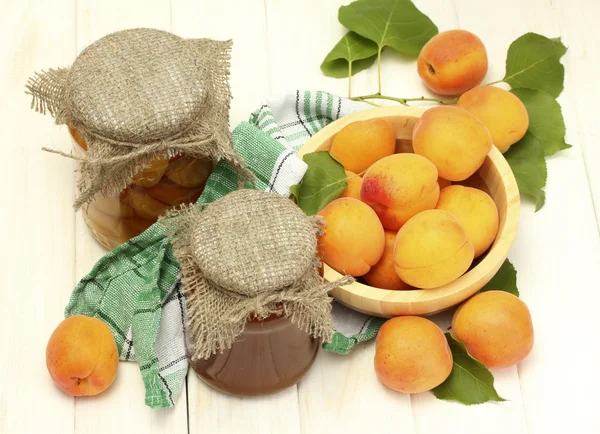 Canned apricots and jam in a jars and ripe apricots in bowl on white wooden — Stock Photo, Image