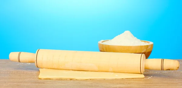The dough with a rolling pin on wooden table on blue background — Stock Photo, Image