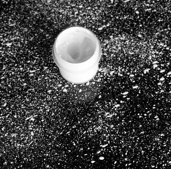 Jar met witte gouache op zwarte achtergrond, spattered met witte verf clos — Stockfoto