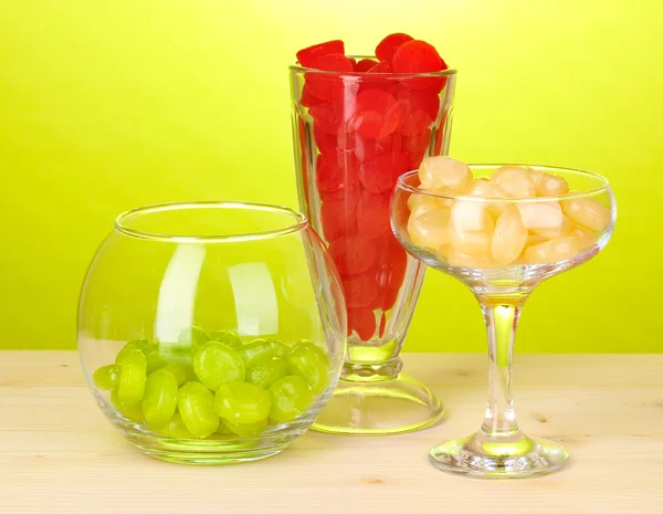 Caramelos de color en vasos sobre mesa de madera sobre fondo verde —  Fotos de Stock