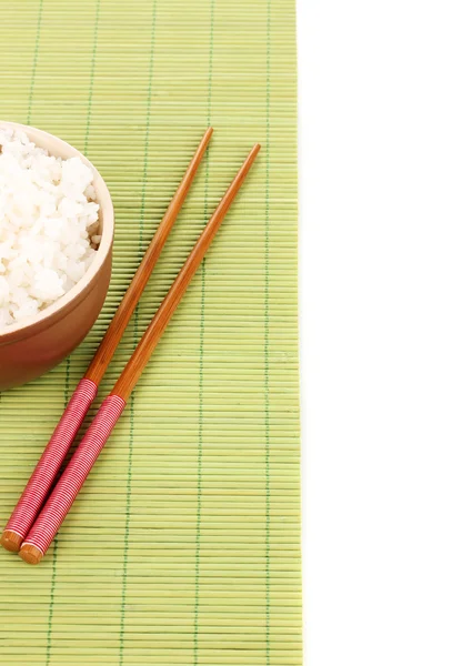 Tigela de arroz e pauzinhos em esteira de bambu isolado em branco — Fotografia de Stock