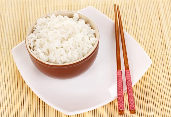 Cuenco de arroz y palillos en el plato en la estera de bambú — Foto de Stock