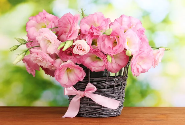 Boeket van eustoma bloemen in rieten vaas, op houten tafel, op groene backg — Stockfoto