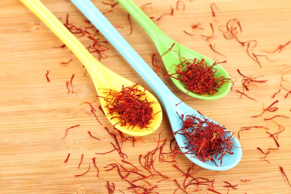 Stigmas of saffron in colorful spoons on wooden background close-up — Stock Photo, Image