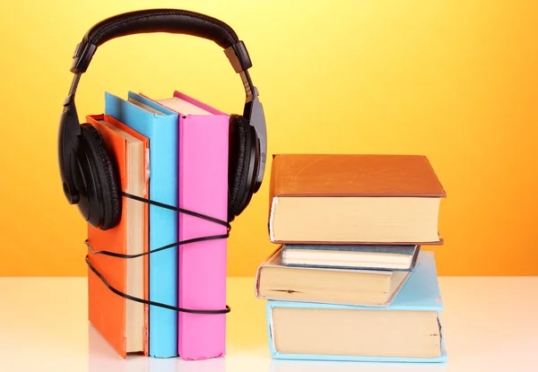 Auriculares en libros sobre fondo naranja — Foto de Stock