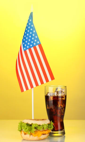 Sanduíche saboroso e cola com bandeira americana, no fundo amarelo — Fotografia de Stock