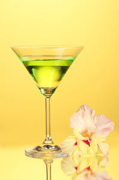 Glass with cocktail and gladiolus bud on yellow background close-up — Stock Photo, Image