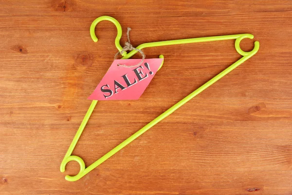 Coat hanger with sale tag on wooden background — Stock Photo, Image