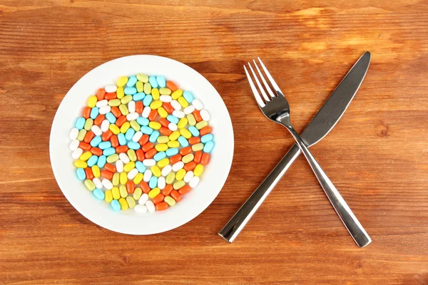 A lot of pills in a plate with knife and fork on wooden background close-up — Stock Photo, Image