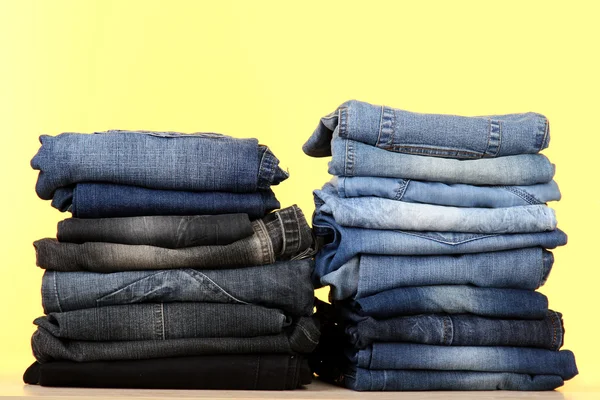 Beaucoup de jeans empilés dans un tas sur fond jaune — Photo