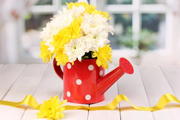 Red watering can of peas with flowers on white wooden table on window back — Stock Photo, Image