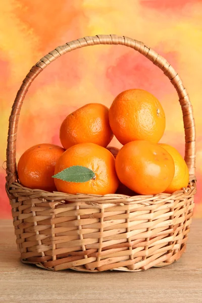 Mandarini con foglie in un bel cesto, su tavolo di legno su bac arancione — Foto Stock