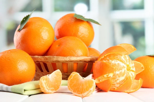 Tangerinas com folhas em uma bela cesta, na mesa de madeira no bac de janela — Fotografia de Stock