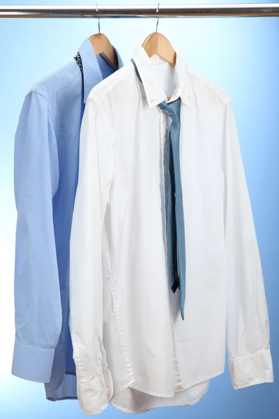 Blue and white shirts with tie on wooden hanger on blue background — Stock Photo, Image