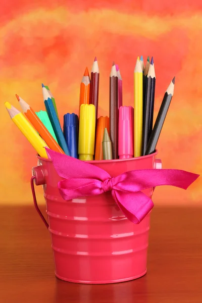 Colorful pencils and felt-tip pens in pink pail on color background — Stock Photo, Image