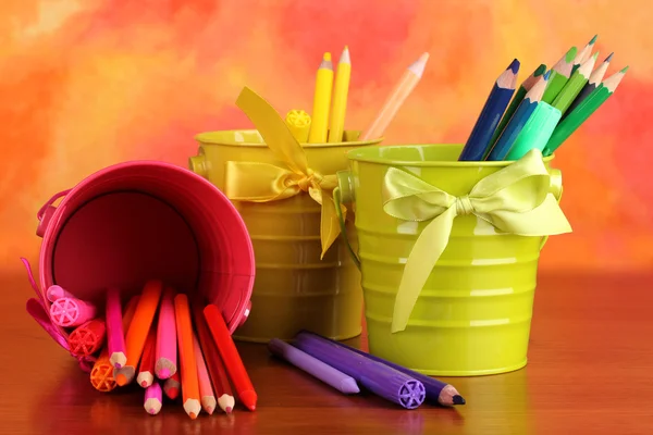 Lápis coloridos e canetas de feltro em baldes sobre fundo de cor — Fotografia de Stock