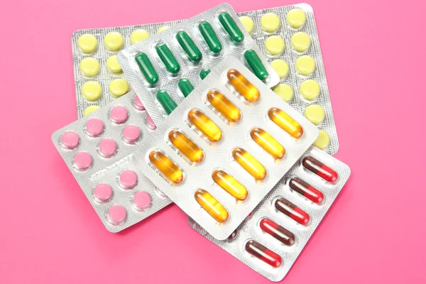 Capsules and pills packed in blisters, on pink background — Stock Photo, Image