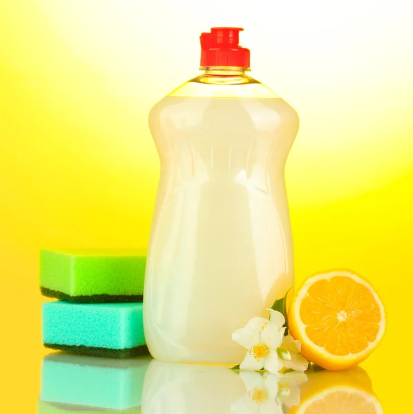 Dishwashing liquid with sponges and lemon with flowers on yellow background — Stock Photo, Image