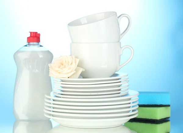 Empty clean plates and cups with dishwashing liquid and sponges on blue bac — Stock Photo, Image