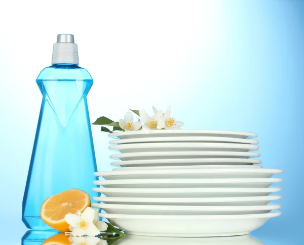Piatti puliti vuoti con detersivo per piatti e limone su fondo blu — Foto Stock