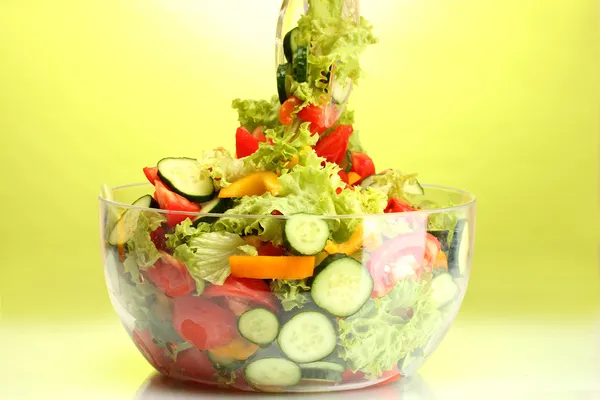 Свежий овощной салат в прозрачной миске с ложкой и вилкой на зеленой спине — стоковое фото