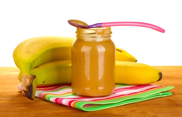 Jar with banana baby food, spoon and bananas on colorful napkin on white ba — Stock Photo, Image