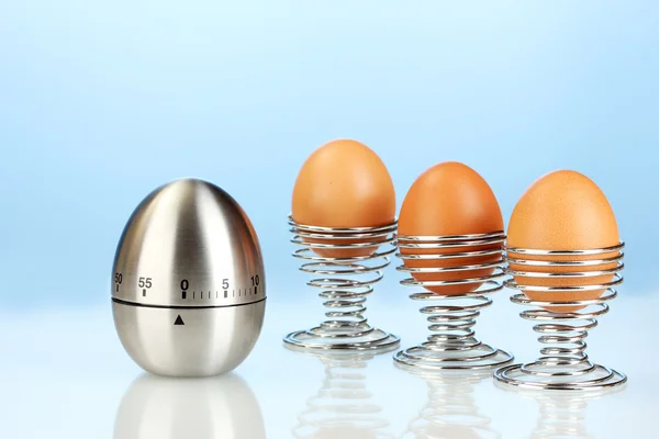 Egg timer and egg in metal stand on blue background — Stock Photo, Image