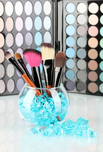 Make-up brushes in a bowl with stones on palette of shadows background — Stock Photo, Image