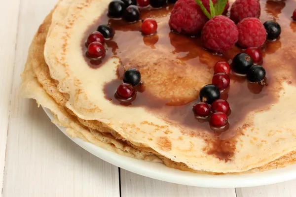 Delicious pancakes with berries and chocolate on plate on wooden table — Stock Photo, Image