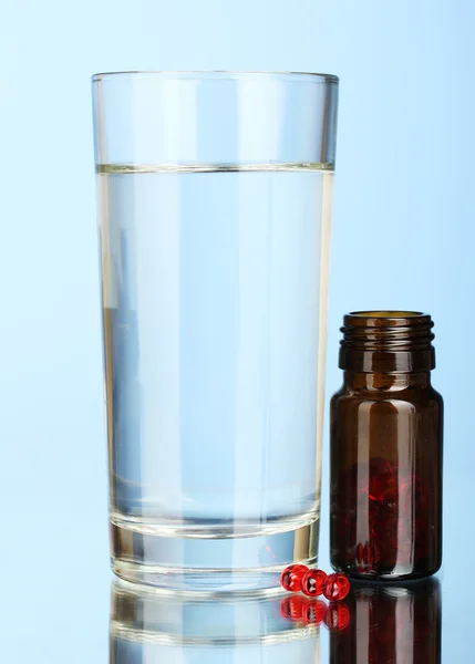 Szklanką wody i tabletki na niebieskim tle z bliska — Zdjęcie stockowe