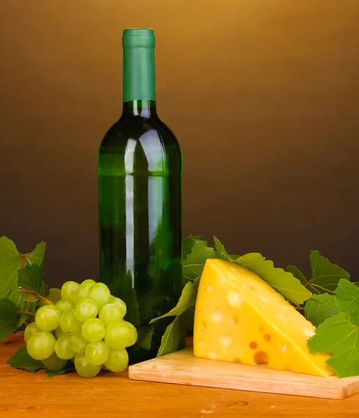 Fles van grote wijn en kaas op houten tafel op bruine achtergrond — Stockfoto