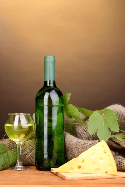 Flasche großer Wein mit Glas und Käse auf Holztisch auf braunem Hintergrund — Stockfoto