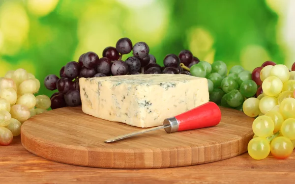 Cheese with mold on the cutting board with grapes on bright green backgroun — Stock Photo, Image