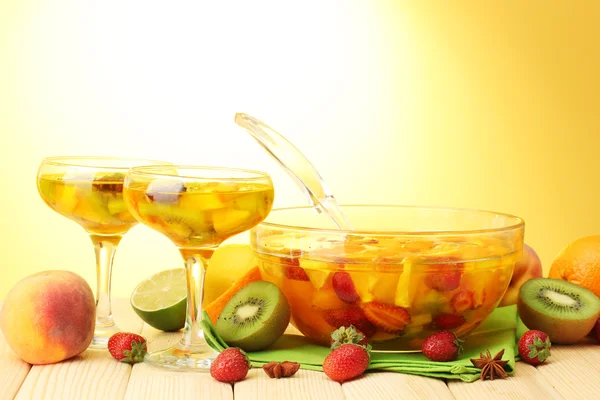 Punch in bowl and glasses with fruits, on wooden table, on yellow backgroun — Stock Photo, Image