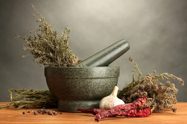 Ervas secas em argamassa e legumes, sobre mesa de madeira sobre fundo cinzento — Fotografia de Stock