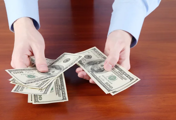 Man vertelt dollars op een houten tafel close-up — Stockfoto