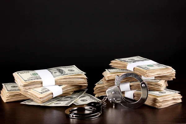 Handcuffs and packs of dollars on wooden table close-up — Stock Photo, Image