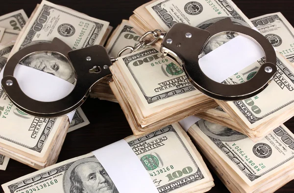 Handcuffs and packs of dollars on wooden table close-up — Stock Photo, Image