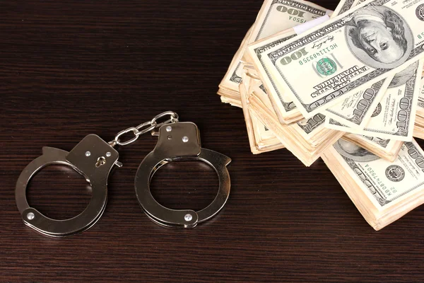 Handcuffs and packs of dollars on wooden table close-up — Stock Photo, Image